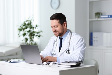 Smiling doctor having online consultation via laptop at table in clinic