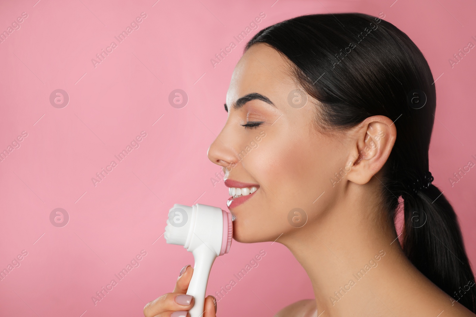 Photo of Young woman using facial cleansing brush on pink background, space for text. Washing accessory