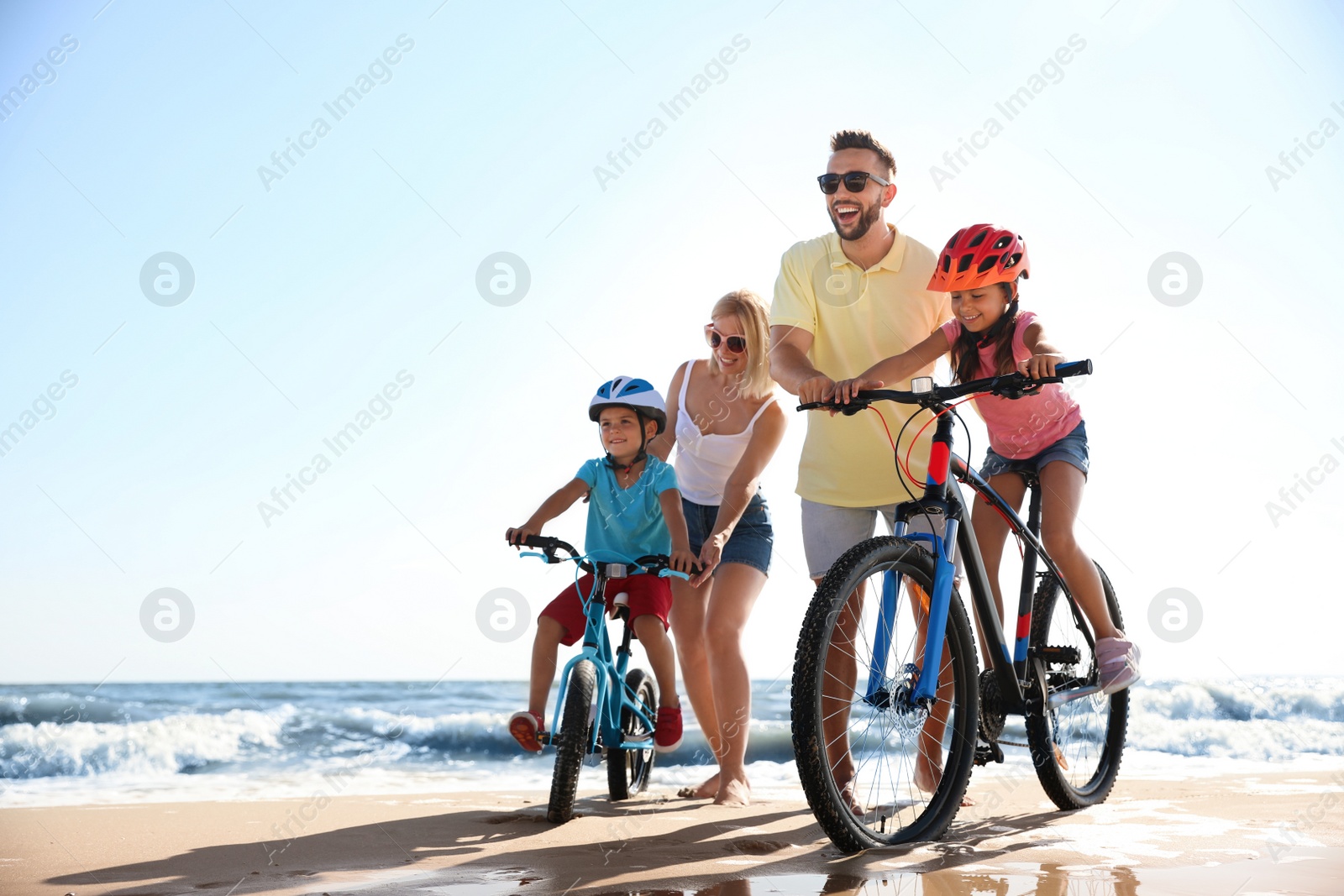 Photo of Happy parents teaching children to ride bicycles on sandy beach near sea