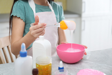 Little girl mixing ingredients with silicone spatula at table in kitchen, closeup. DIY slime toy