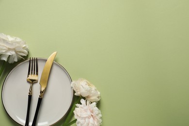 Photo of Stylish table setting with cutlery and flowers on light green background, flat lay. Space for text