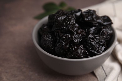Photo of Sweet dried prunes in bowl on brown table, closeup. Space for text