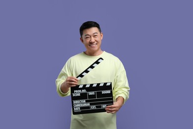Happy asian actor with clapperboard on purple background. Film industry