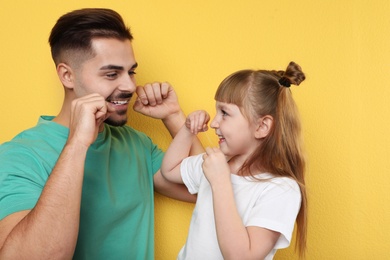 Photo of Little girl and her father flossing teeth on color background