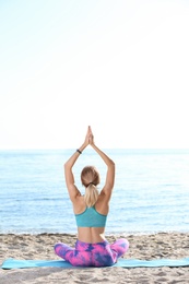 Photo of Young woman doing yoga exercises on beach in morning