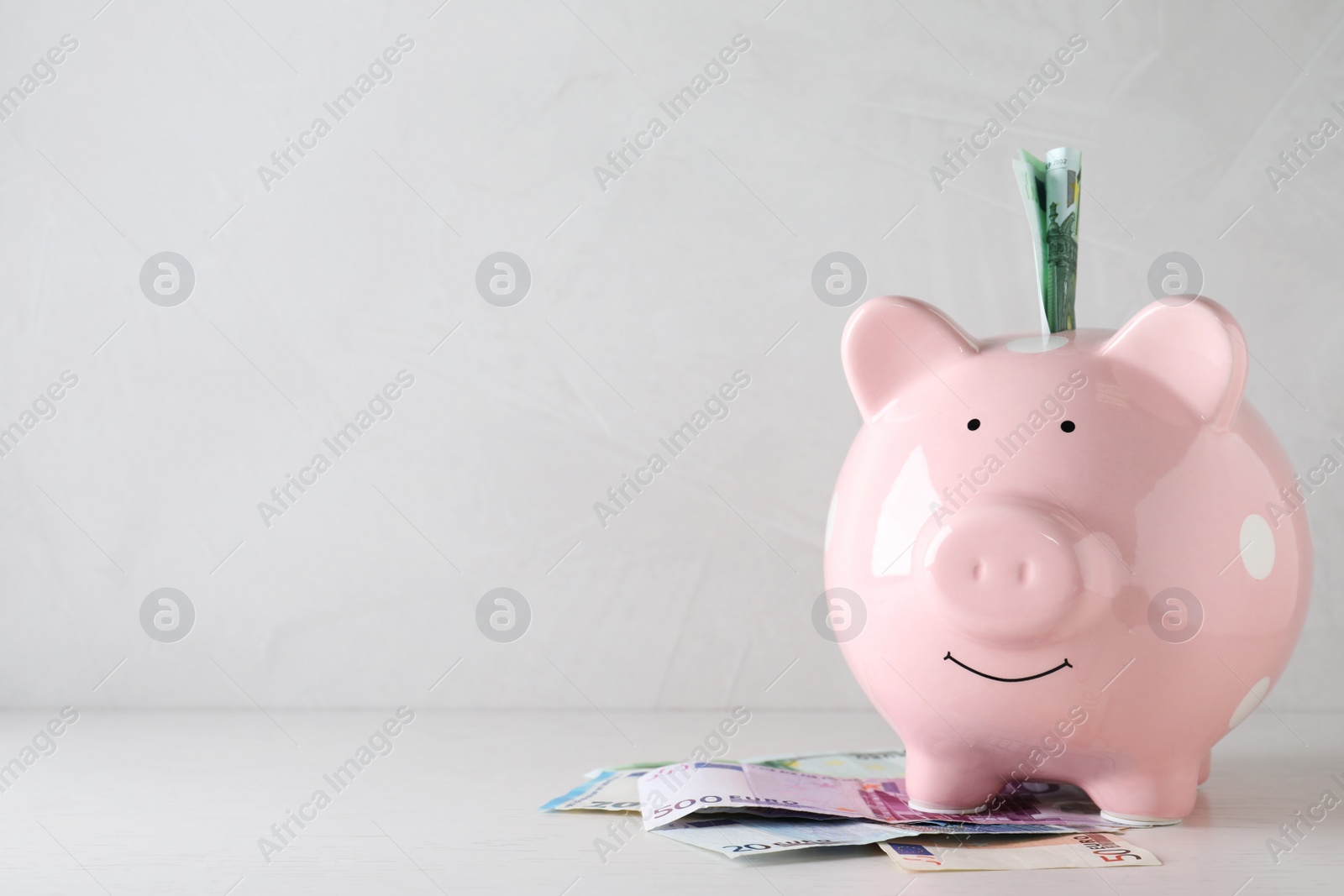 Image of Pink piggy bank with money on light table, space for text