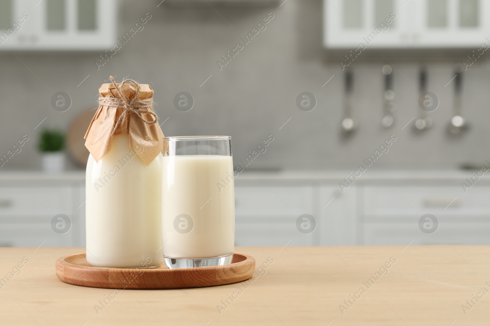 Photo of Bottle and glass with milk on wooden table in kitchen, space for text