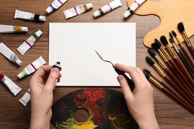 Man with paint, spatula and blank canvas at wooden table, top view