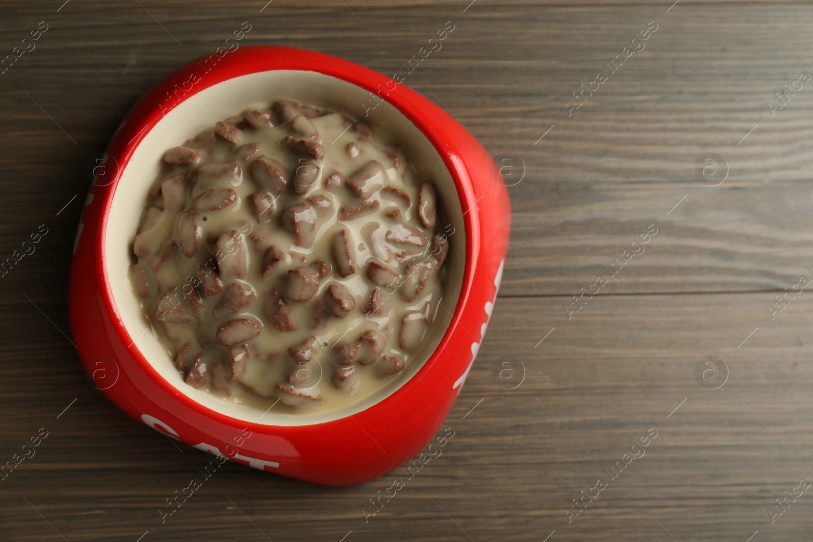 Photo of Wet pet food in feeding bowl on wooden background, top view. Space for text