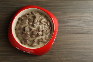 Wet pet food in feeding bowl on wooden background, top view. Space for text