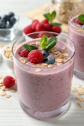 Photo of Tasty smoothie with berries, mint and oatmeal on white wooden table