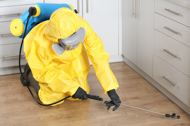 Photo of Pest control worker in protective suit spraying pesticide indoors