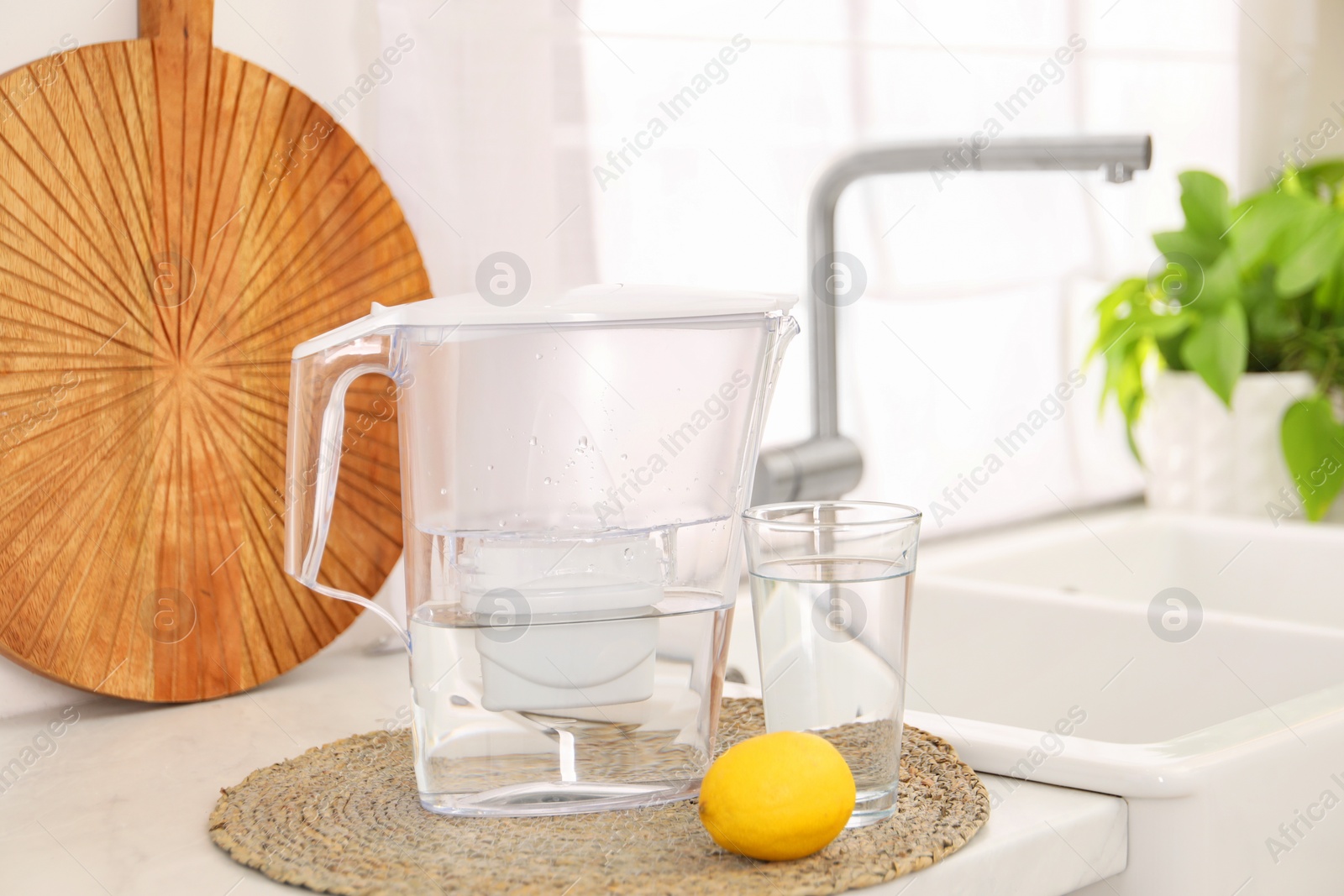 Photo of Water filter jug, glass and lemon on countertop in kitchen