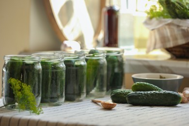 Photo of Set of glass jars with fresh cucumbers and other ingredients prepared for canning on table