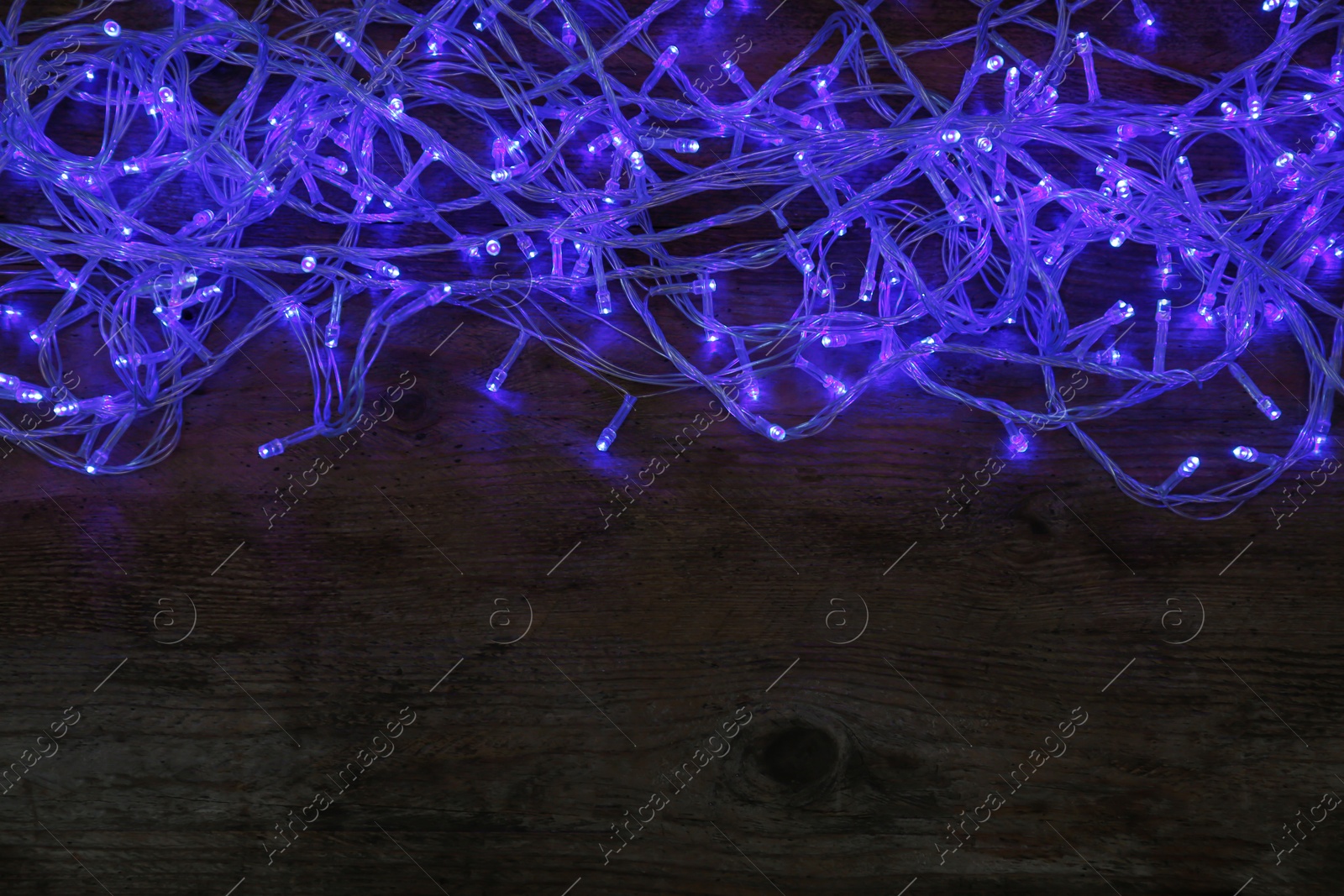 Photo of Blue Christmas lights on wooden background, top view. Space for text