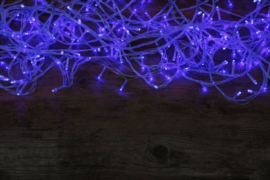 Photo of Blue Christmas lights on wooden background, top view. Space for text