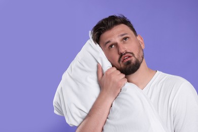Photo of Unhappy man with pillow on violet background, space for text. Insomnia problem