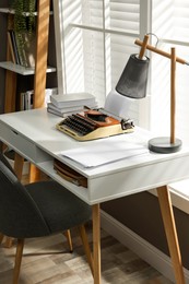 Photo of Comfortable writer's workplace interior with typewriter on desk in front of window