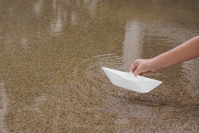 Kid launching small white paper boat on water outdoors, closeup. Space for text