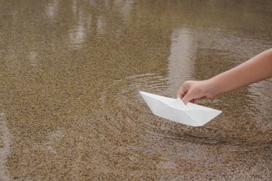 Photo of Kid launching small white paper boat on water outdoors, closeup. Space for text