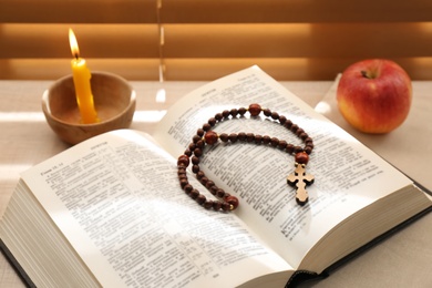 Photo of Bible with prayer beads, candle and apple near window indoors. Great Lent season