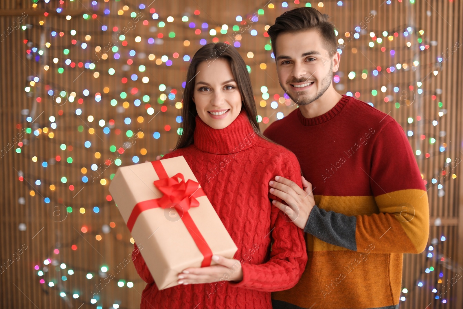 Photo of Young couple with Christmas gift on blurred lights background