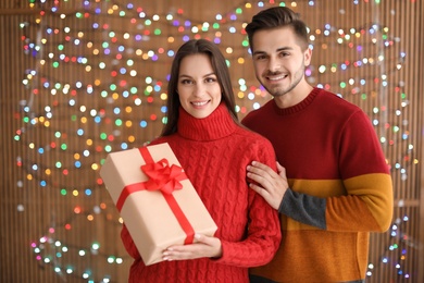 Young couple with Christmas gift on blurred lights background