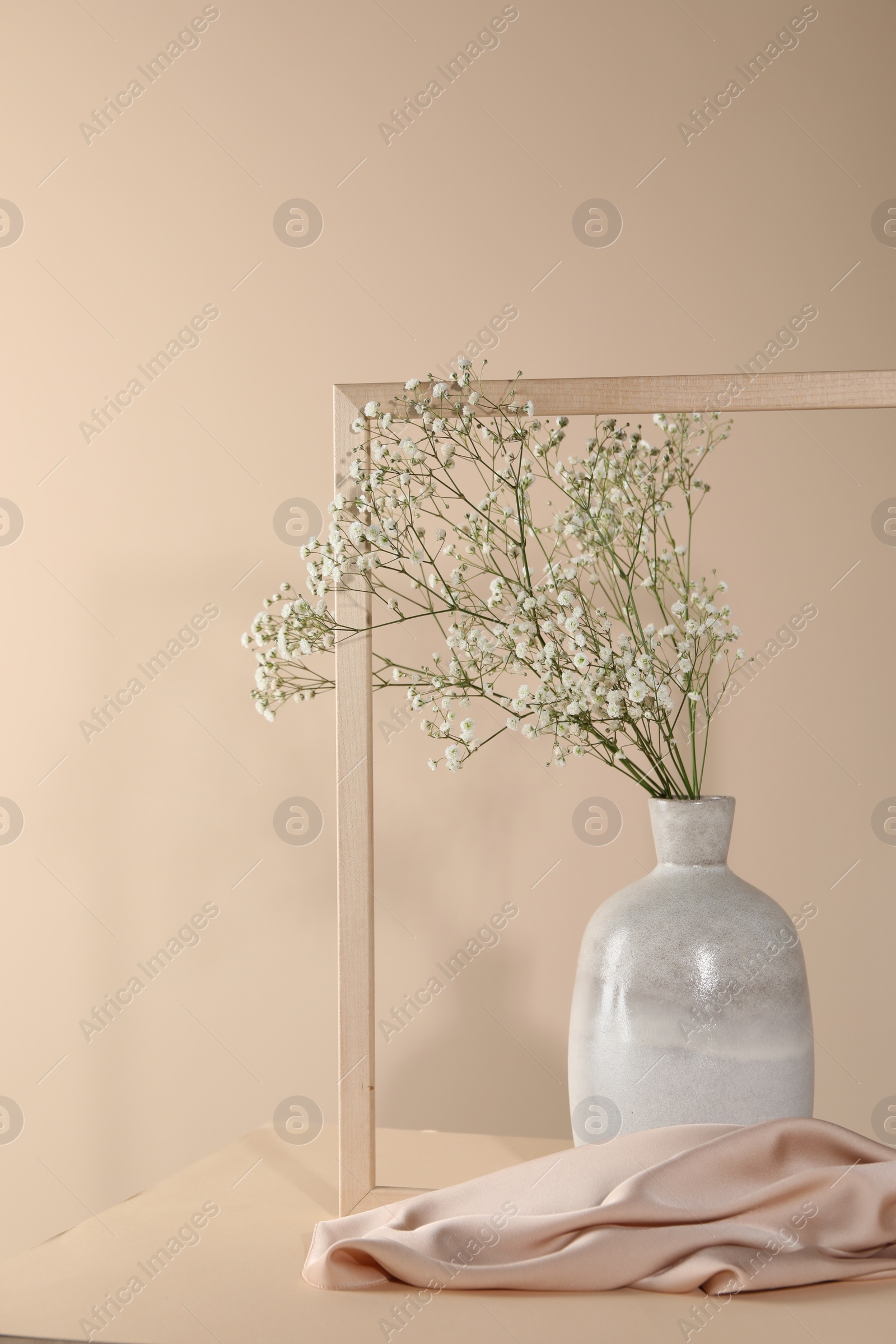 Photo of Vase with flowers, picture frame and cloth on wooden table against beige background