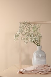 Vase with flowers, picture frame and cloth on wooden table against beige background