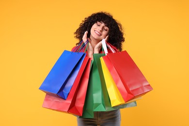 Happy young woman with shopping bags on yellow background