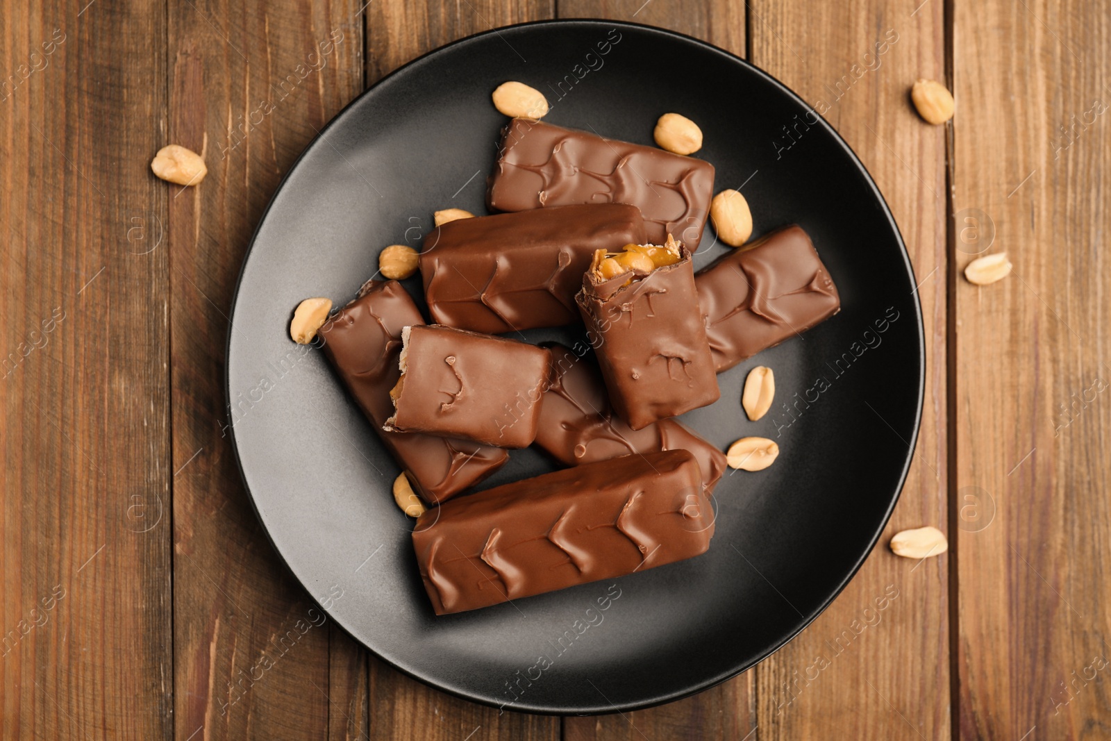 Photo of Plate of chocolate bars with caramel, nuts and nougat on wooden table, top view