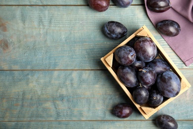 Delicious ripe plums in crate on blue wooden table, flat lay. Space for text