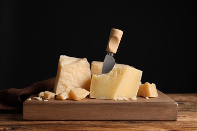 Photo of Parmesan cheese with board and knife on wooden table