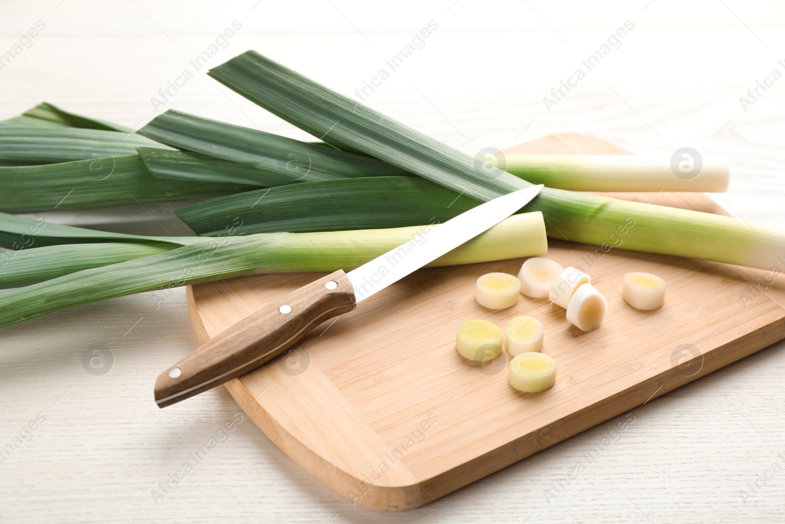 Photo of Fresh leeks and knife on white wooden table