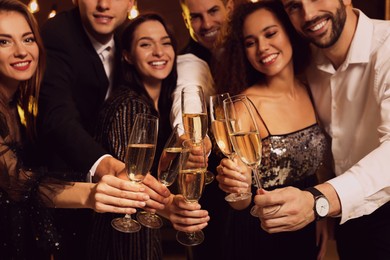 Photo of Happy friends celebrating New Year indoors, focus on hands with glasses of sparkling wine 