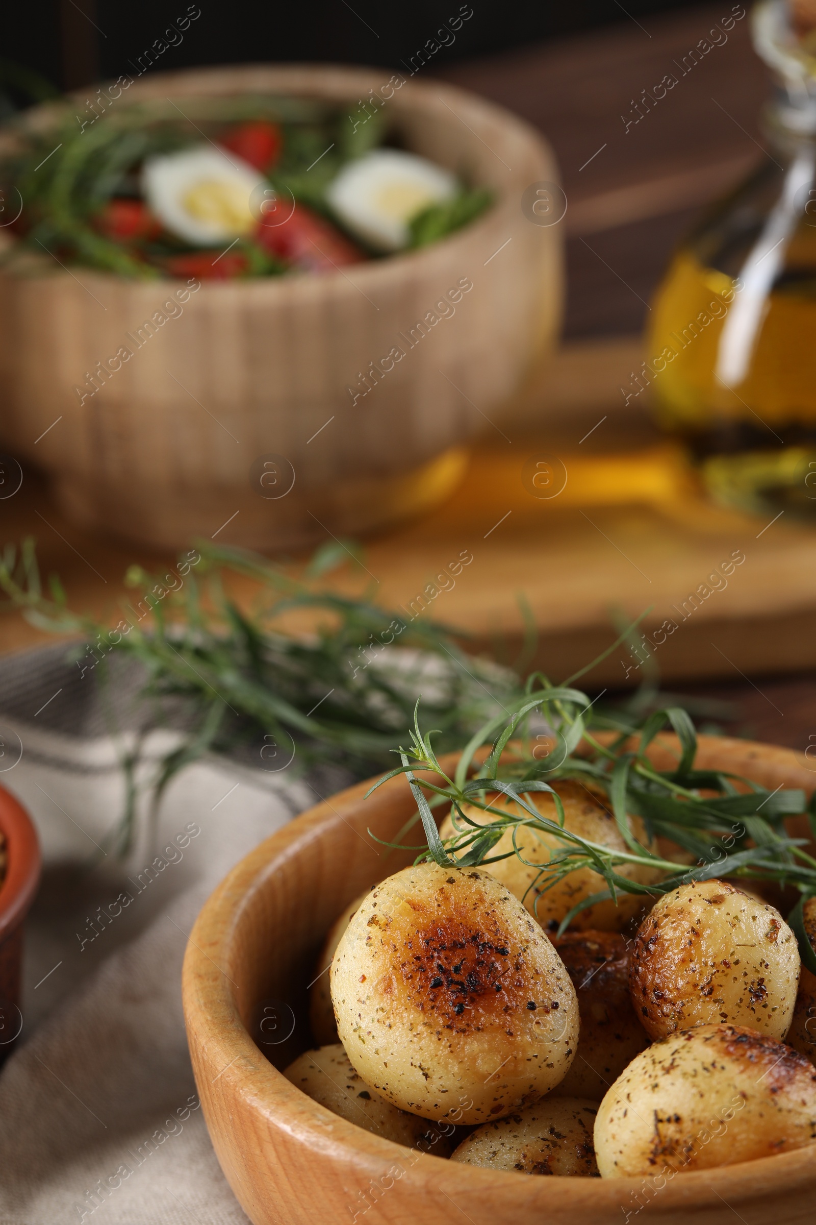 Photo of Delicious grilled potatoes with tarragon and salad on table, selective focus