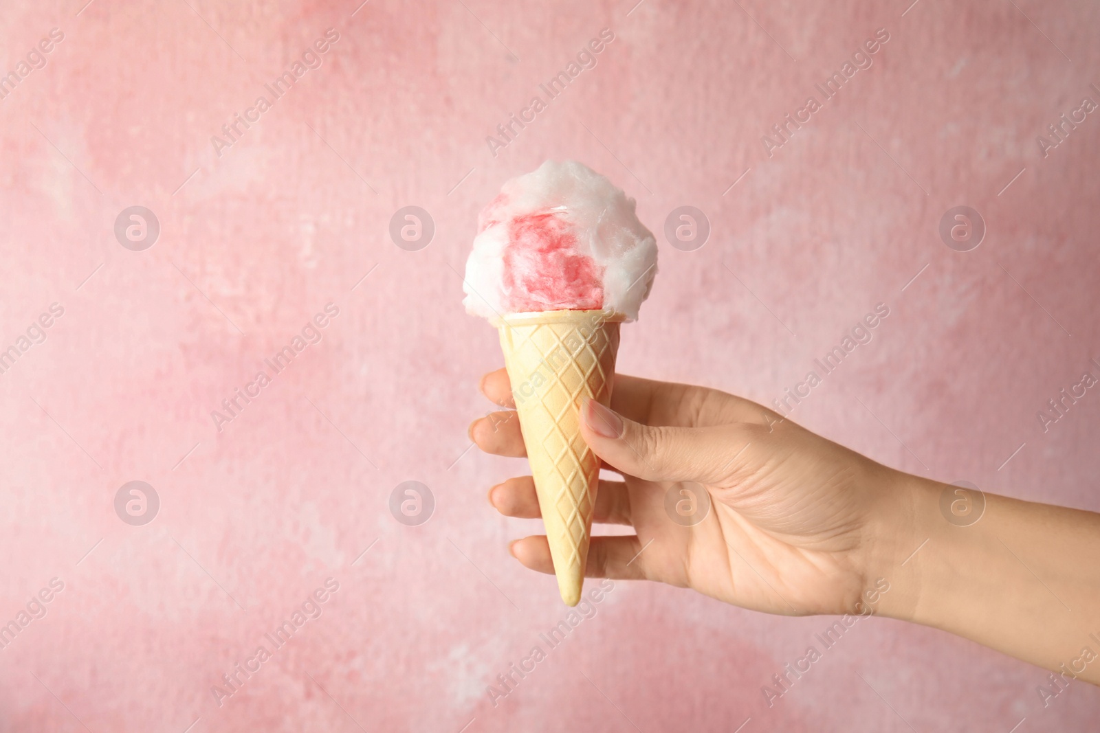 Photo of Woman holding ice cream cone with fluffy cotton candy on color background, closeup