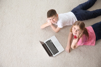 Photo of Teenage girl and her brother with laptop lying on cozy carpet at home