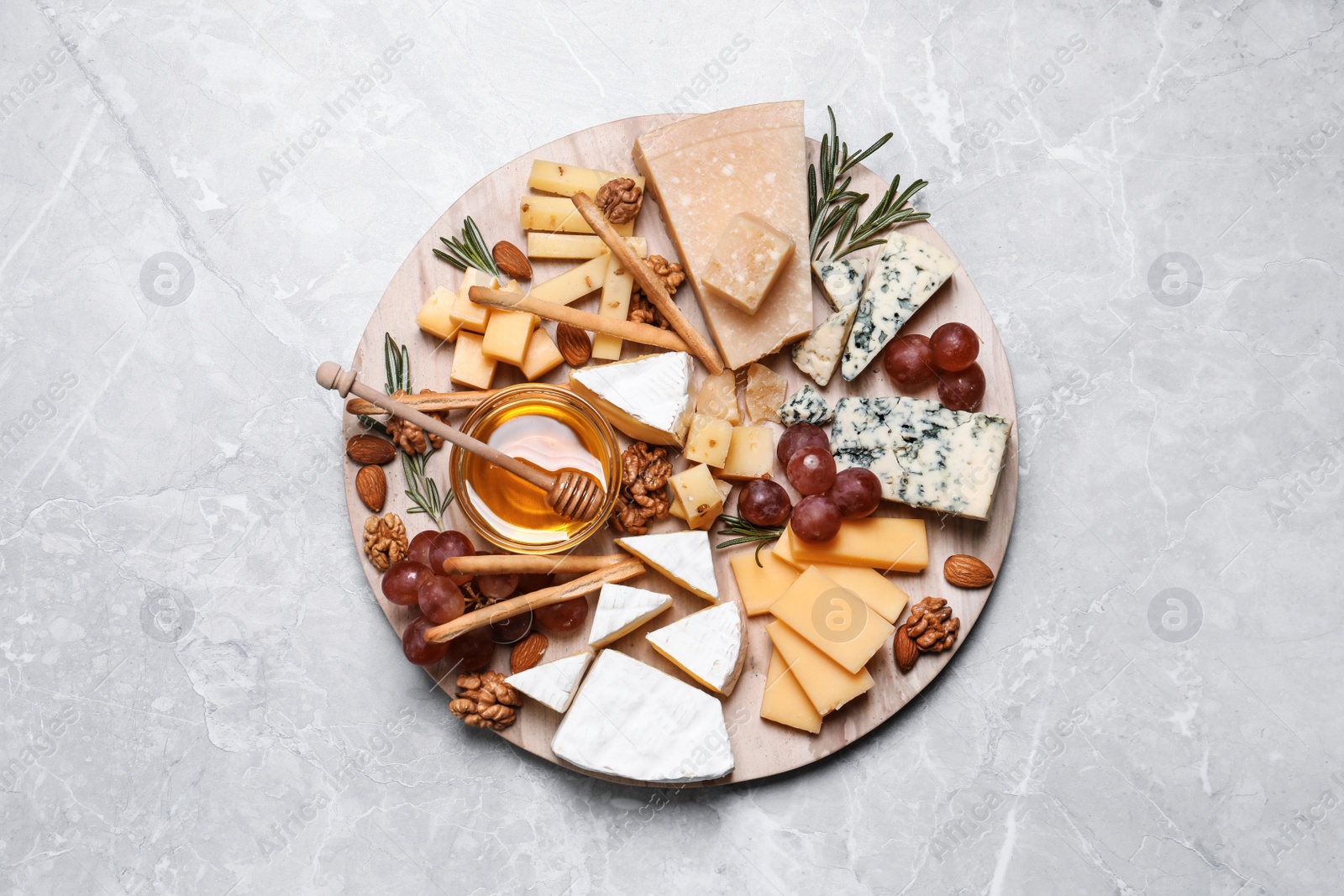 Photo of Cheese plate with honey, grapes and nuts on light grey marble table, top view