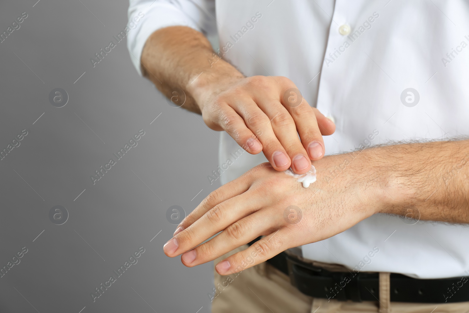 Photo of Man applying cream onto hand on grey background, closeup. Space for text