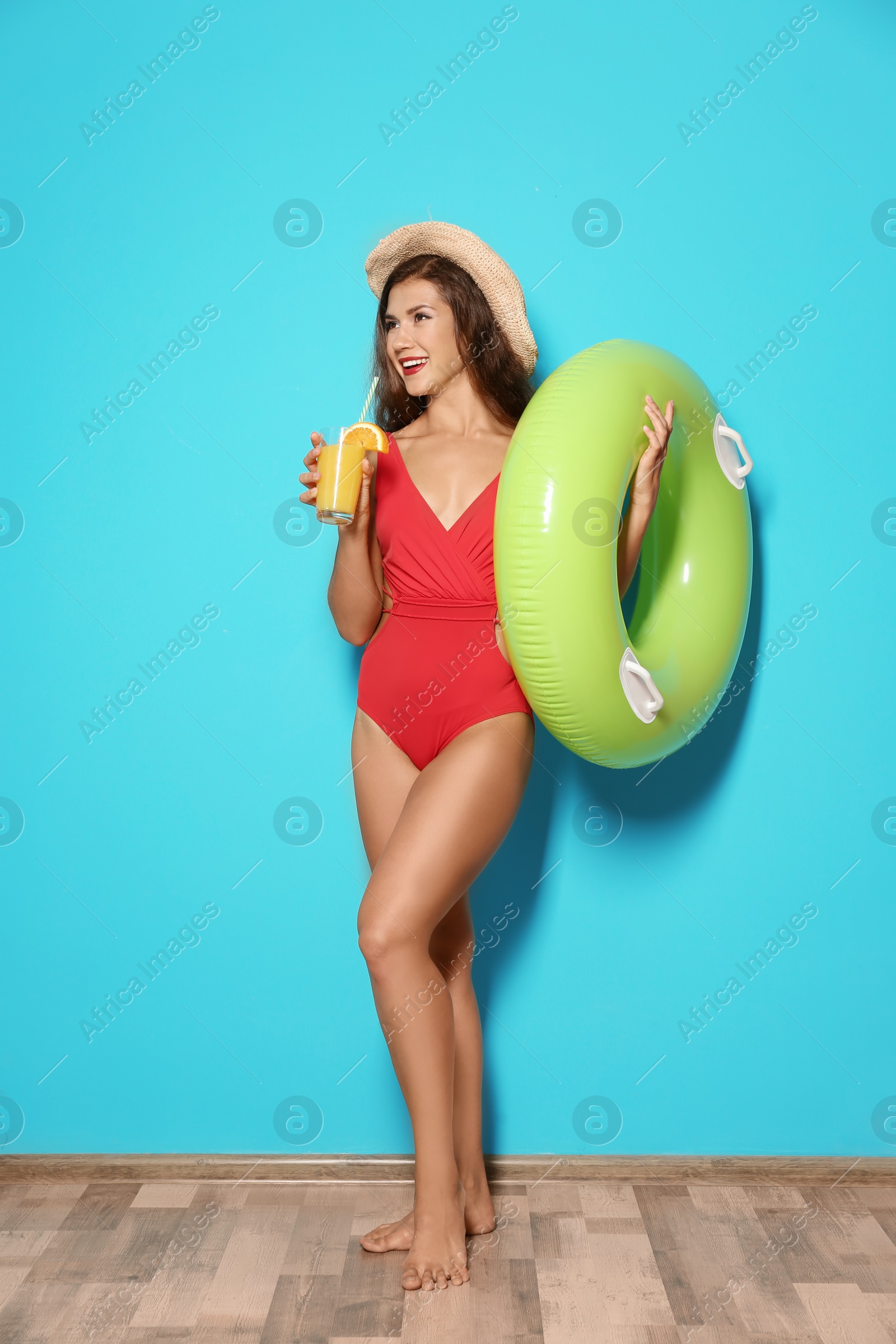 Photo of Beautiful young woman with inflatable ring and glass of cocktail near color wall