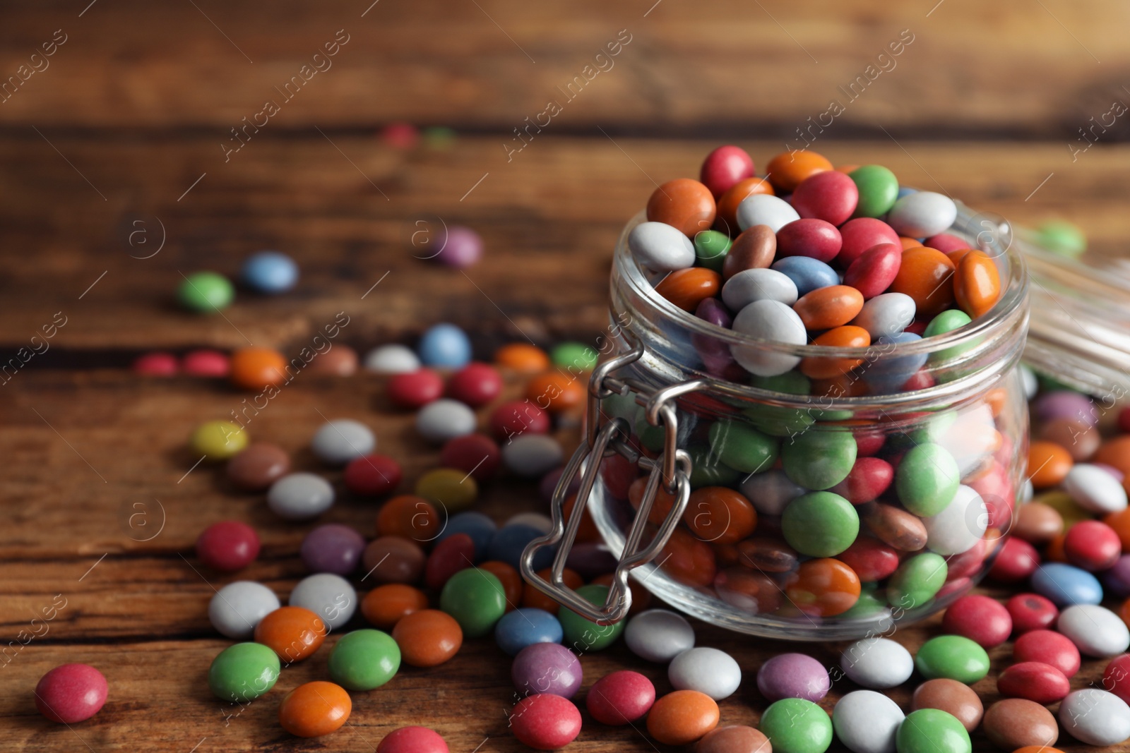 Photo of Delicious dragee in jar on wooden table, closeup. Space for text