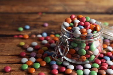 Photo of Delicious dragee in jar on wooden table, closeup. Space for text