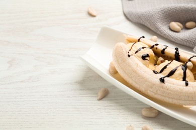 Delicious banana split ice cream with chocolate topping and peanuts on white wooden table, closeup. Space for text