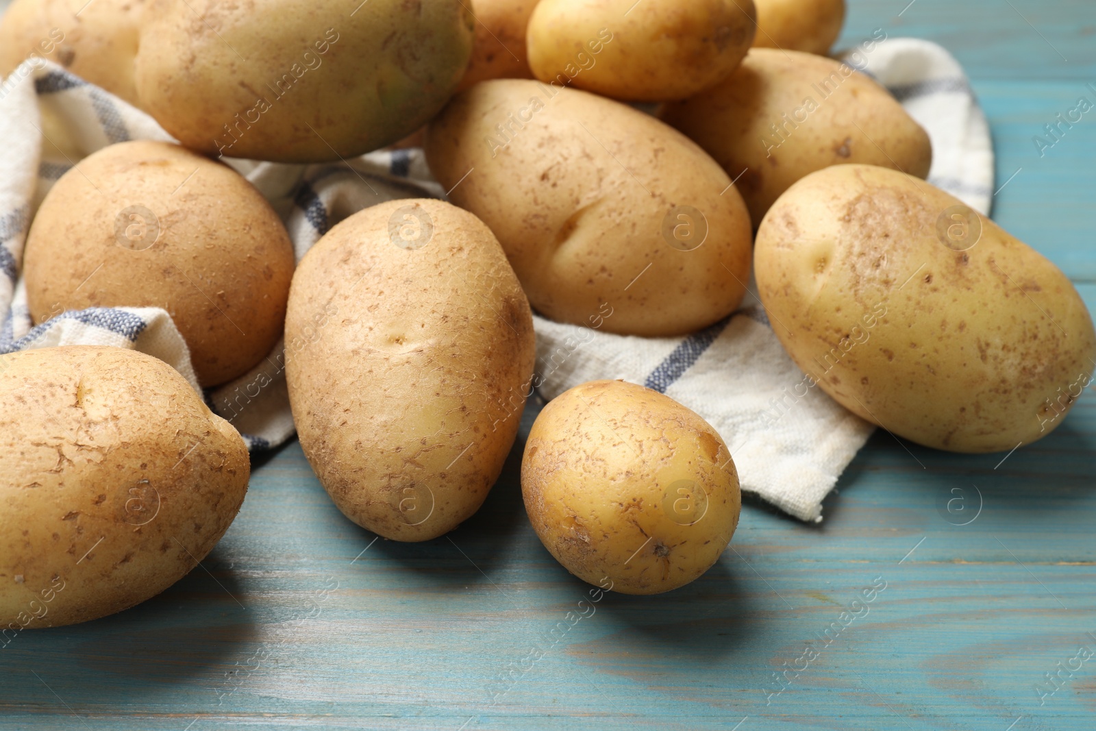 Photo of Raw fresh potatoes and napkin on light blue wooden table