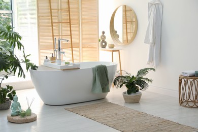 Stylish bathroom interior with modern tub, window and beautiful houseplants. Home design