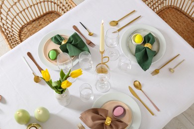 Photo of Festive Easter table setting with painted eggs, burning candles and yellow tulips, view from above