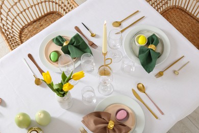 Festive Easter table setting with painted eggs, burning candles and yellow tulips, view from above