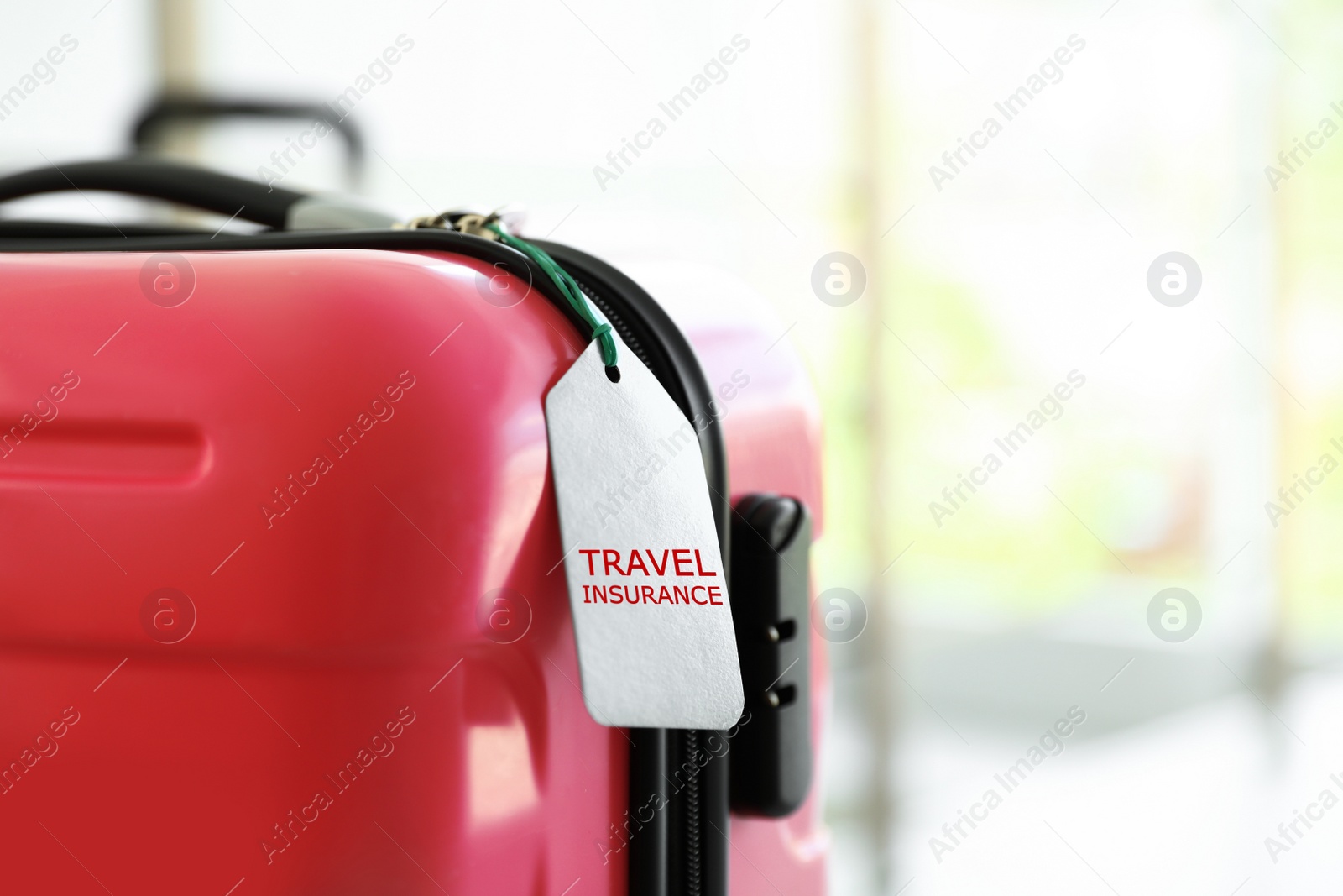 Photo of Stylish suitcase with travel insurance label on blurred background, closeup. Space for text