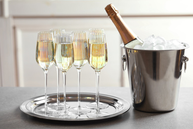 Photo of Glasses of champagne and ice bucket with bottle on grey table